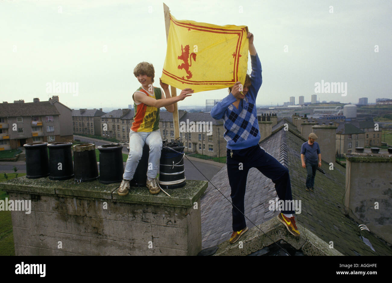 Young kids hold a Scottish flag, the Rampant Lion flag of Scotland above their heads from the roof tops of a huge council block of flats Glasgow 1980s Stock Photo