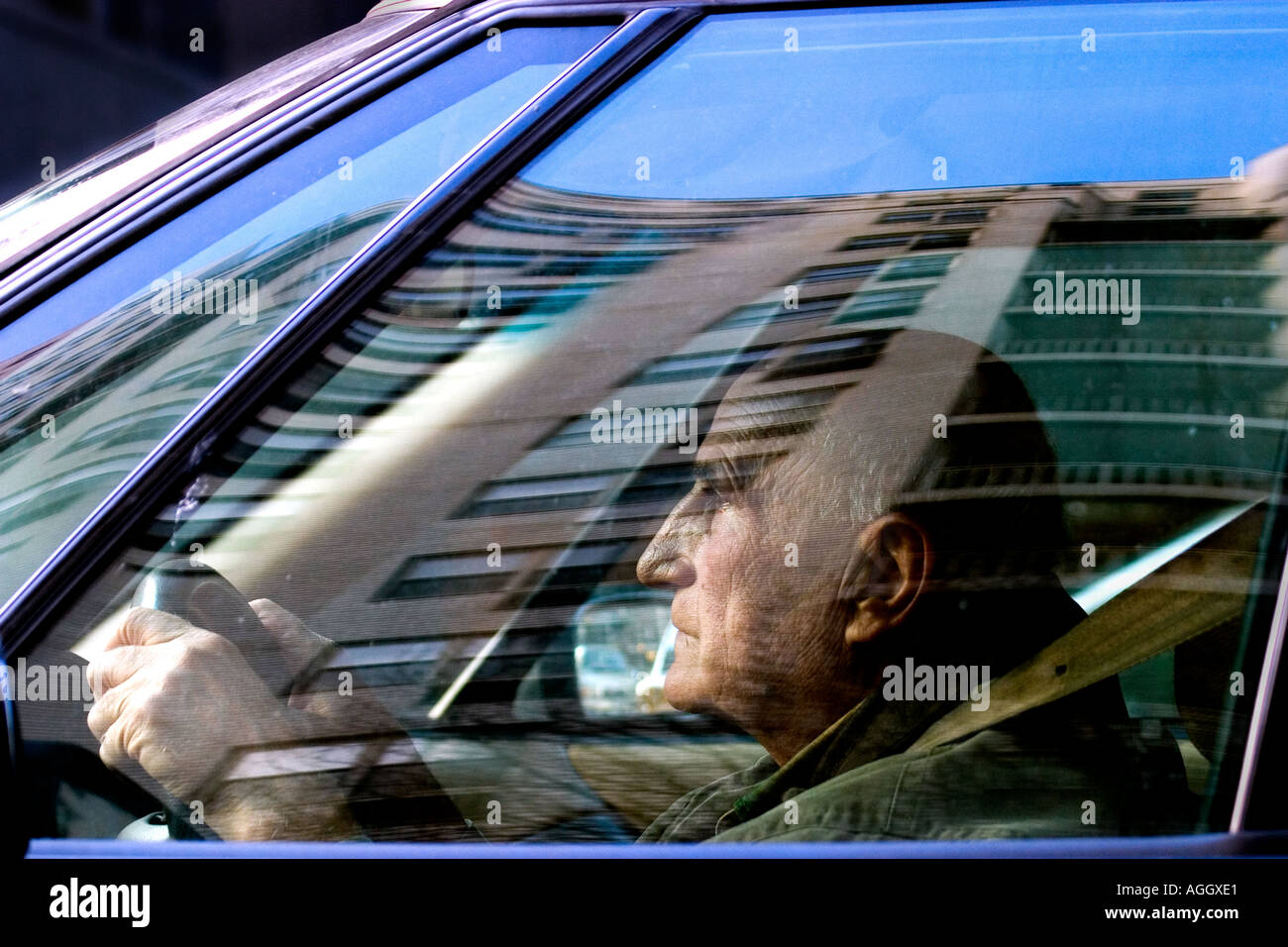 old man driving car shot through window reflecting surrounding buildings as he drives in big urban city New York Stock Photo