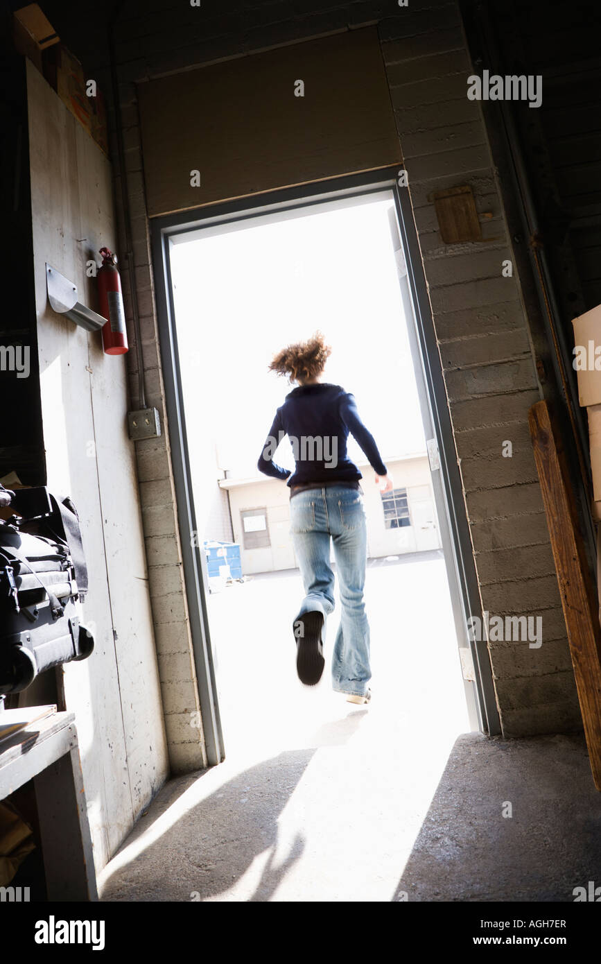 Woman running through open door from building to sunny outside Stock