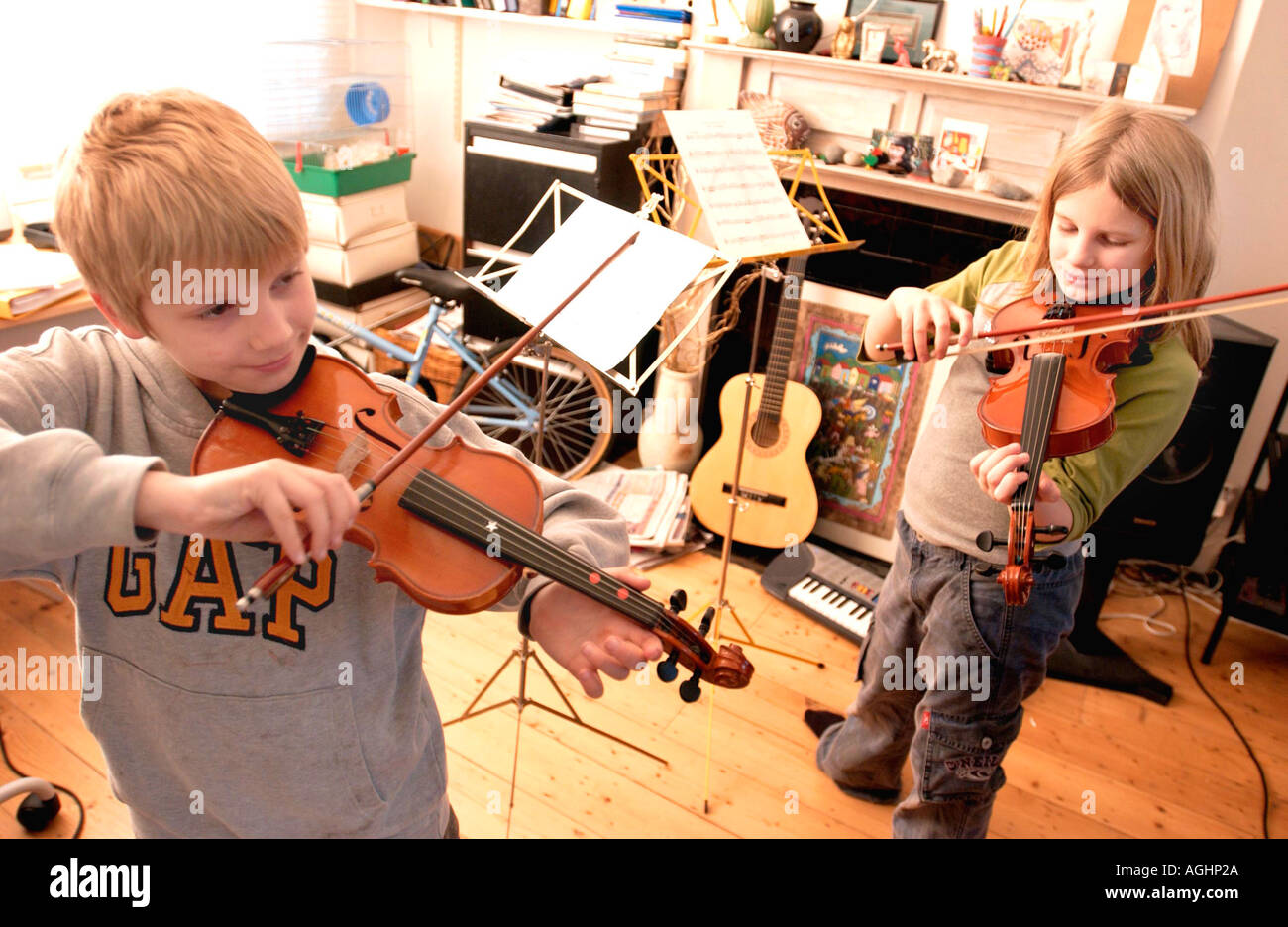 A brother and sister do their daily violin practice in a crowded typical middle class English family living room Stock Photo