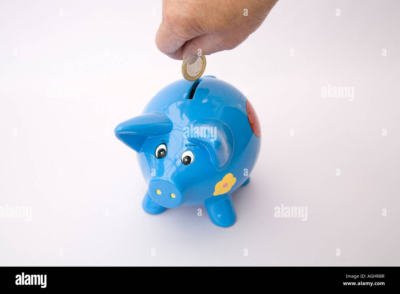 STUDIO Putting a £2 coin in a blue piggy bank for a rainy day Stock Photo