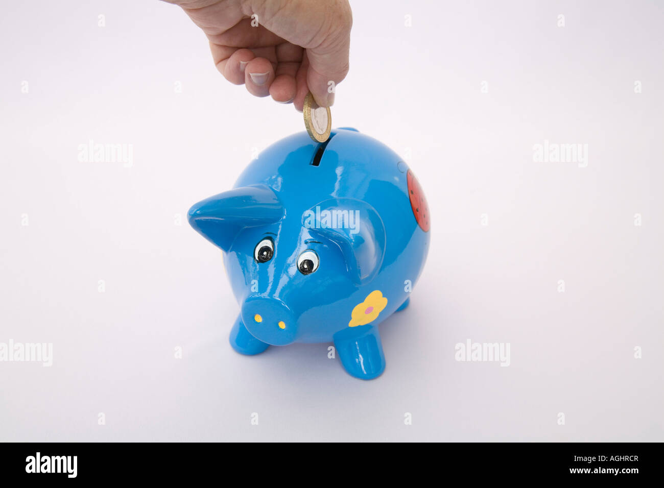STUDIO Putting a £2 coin in a blue piggy bank for a rainy day Stock Photo