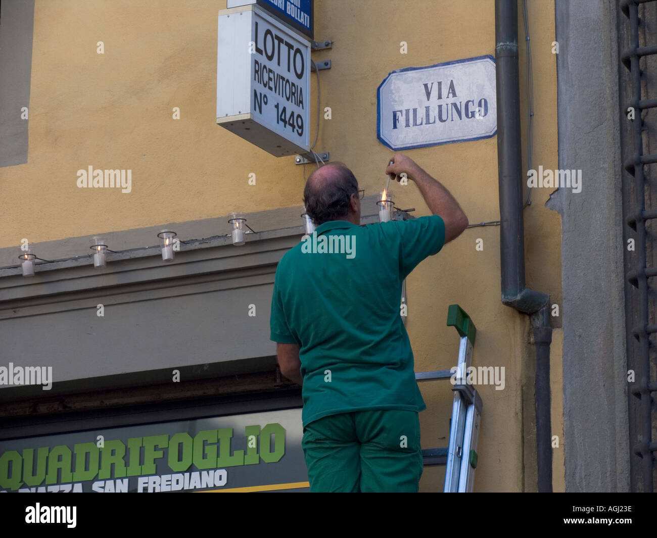 Volunteer lighting candles on buildings along via Fillungo in preparation for religious festival and parade in Lucca Tuscany I Stock Photo
