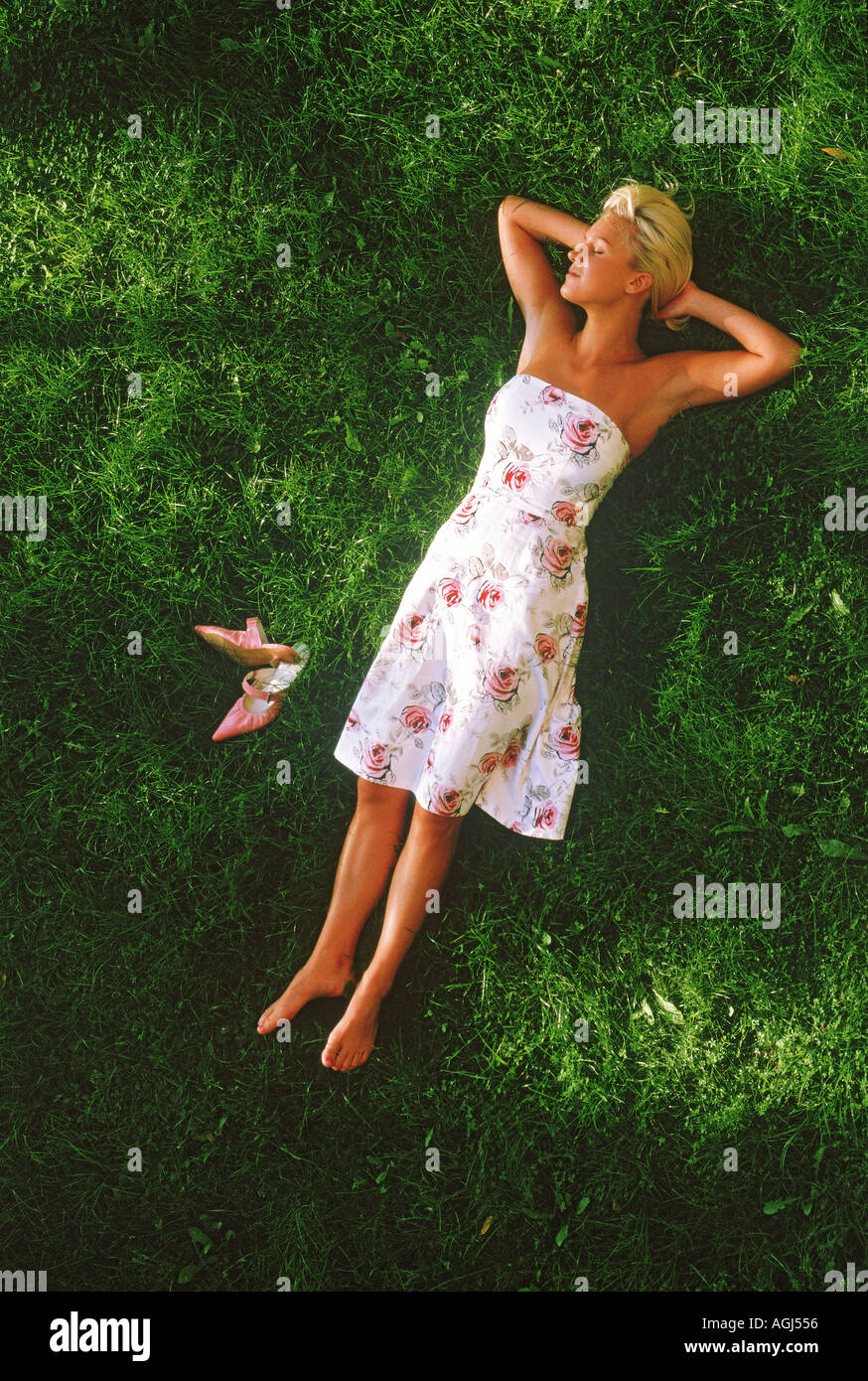 Young blond woman resting barefoot on grass in summer dress Stock Photo Alamy