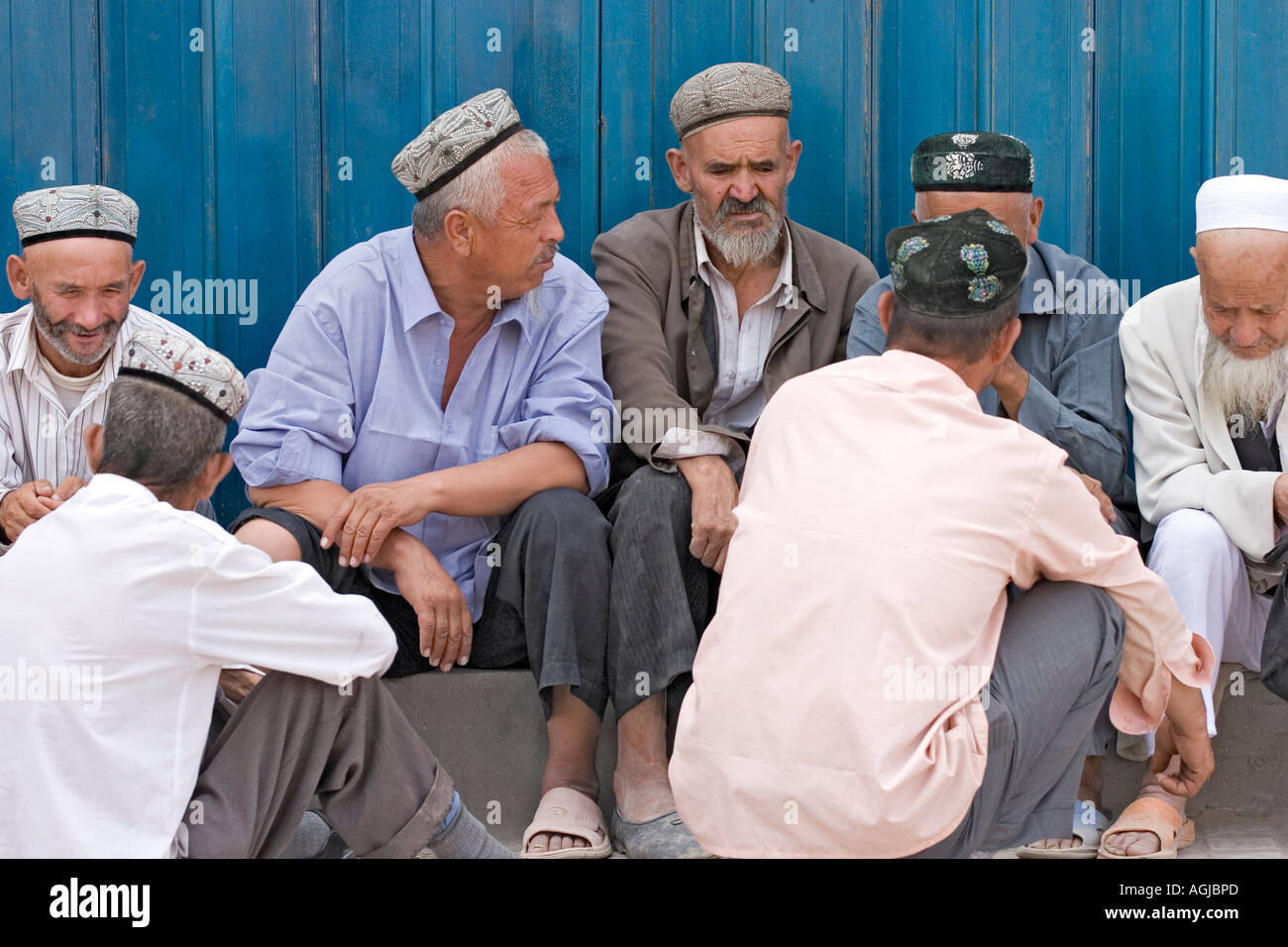 asia china group of old men sitting in front of blue wall on the market of khotan at silkroad Stock Photo