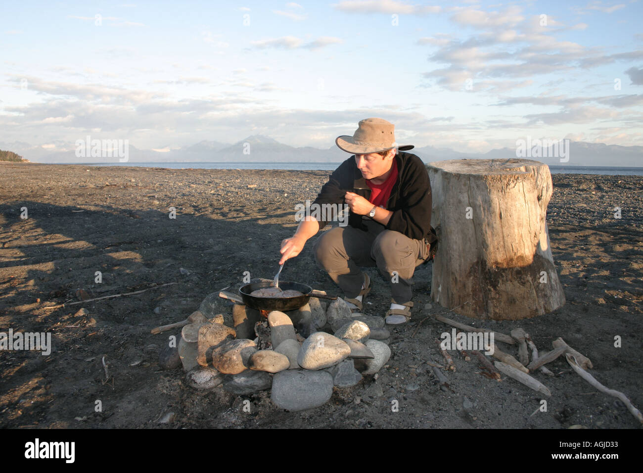 MR a woman cooks a steak on the open fire with a iron cast pan Homer Alaska USA Stock Photo