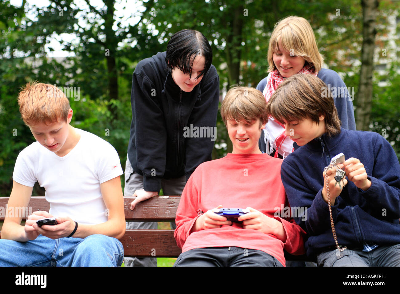 teenagers playing with their gameboys and mobile phones at a park Stock Photo