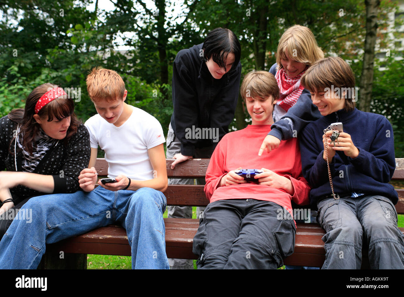 teenagers playing with their gameboys and mobile phones at a park Stock Photo