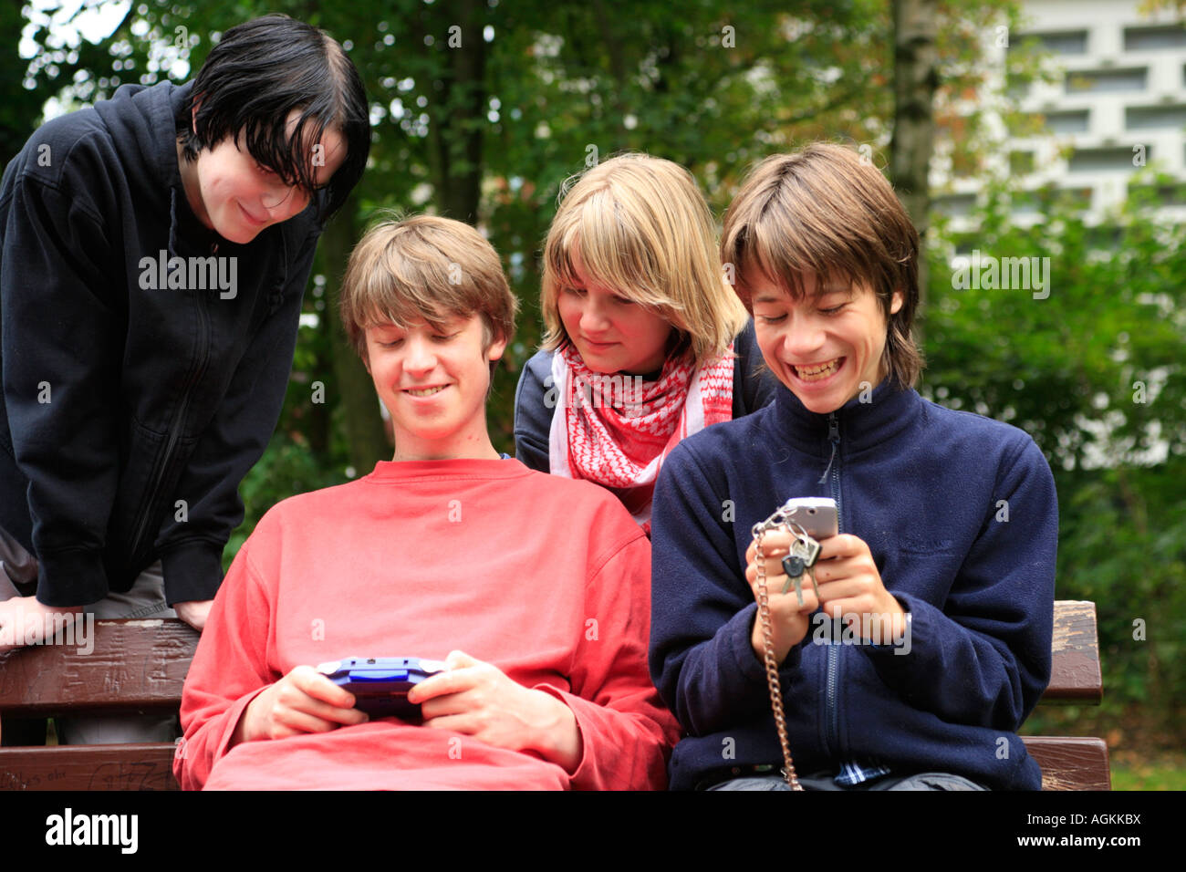 teenagers playing with their gameboys and mobile phones at a park Stock Photo