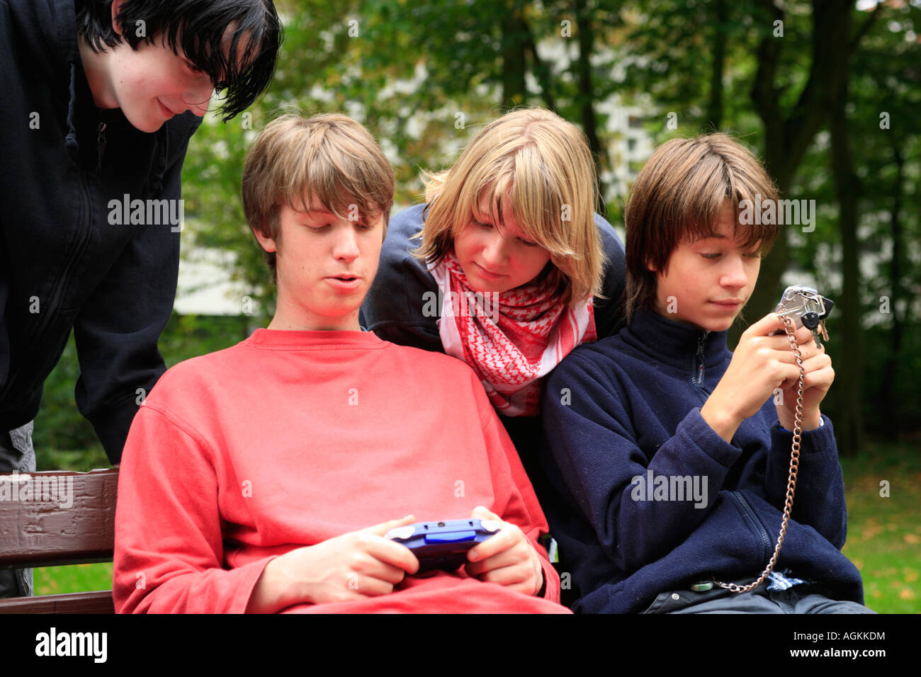 teenagers playing with their gameboys and mobile phones at a park Stock Photo