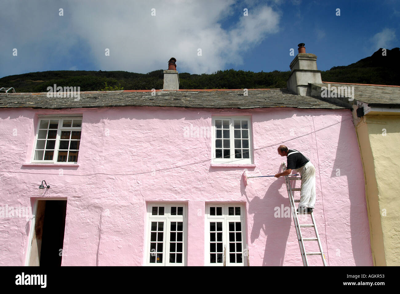A man painting colourful Cornwall cottages standing up a high ladder Stock Photo