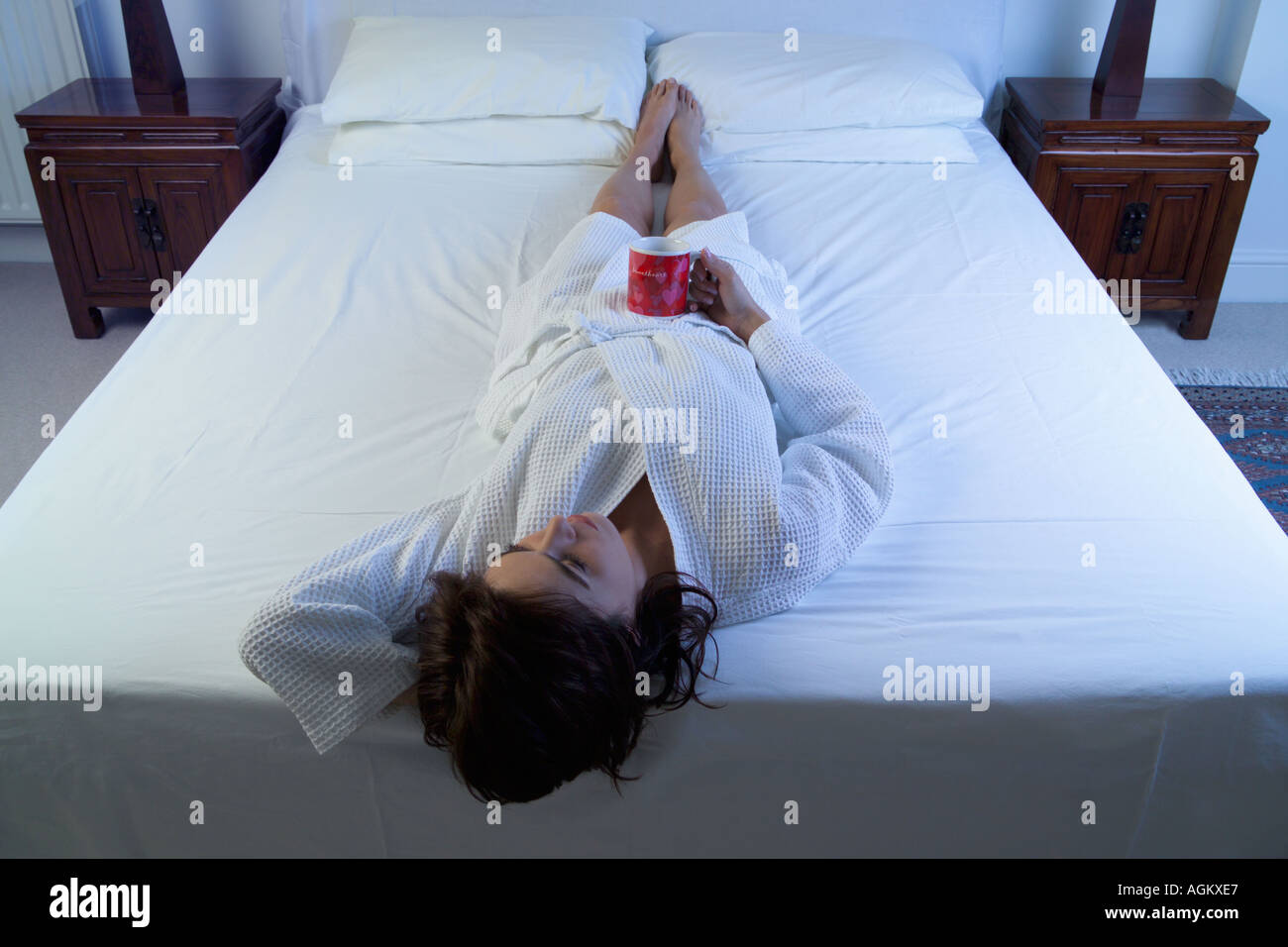 thoughtful girl on bed holds mug Stock Photo Alamy