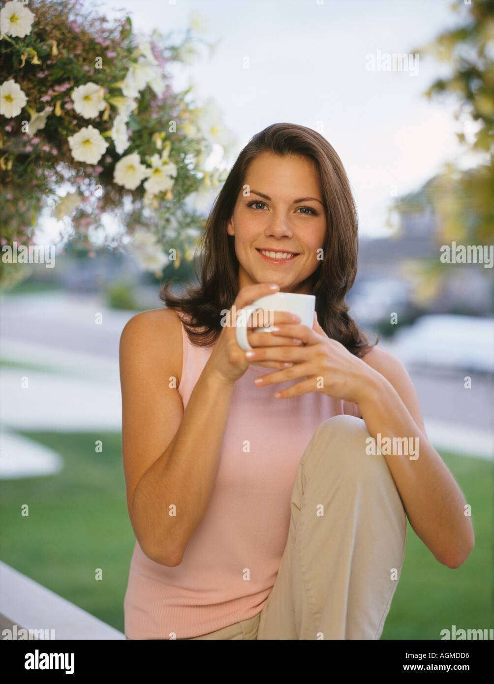 Young woman sitting on porch railing drinking hot beverage Stock Photo