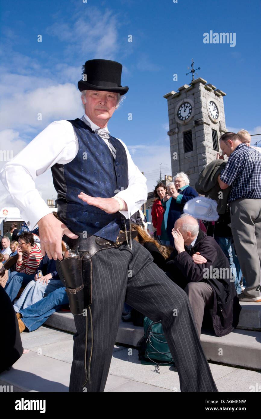 Scottish events Creetown Country Music Festival cowboy posing with gun in the Square with clocktower behind Galloway Scotland UK Stock Photo