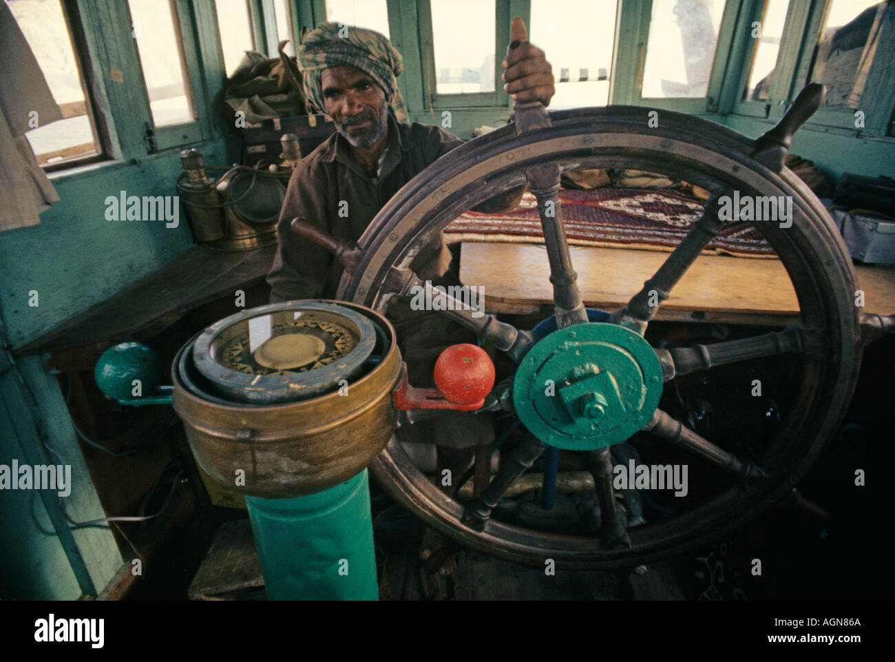 Helmsman at the wheel of an Arab dhow in Persian Gulf waters steering by the compass Stock Photo