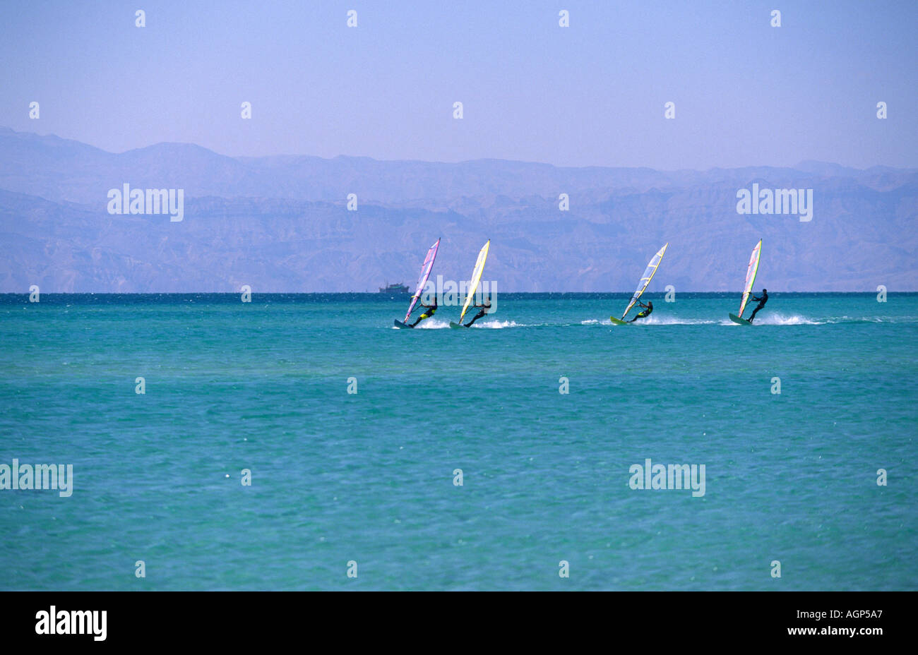 Four windsurfers appearing small as they sail fast, far out on the Red Sea Sinai Egypt Stock Photo