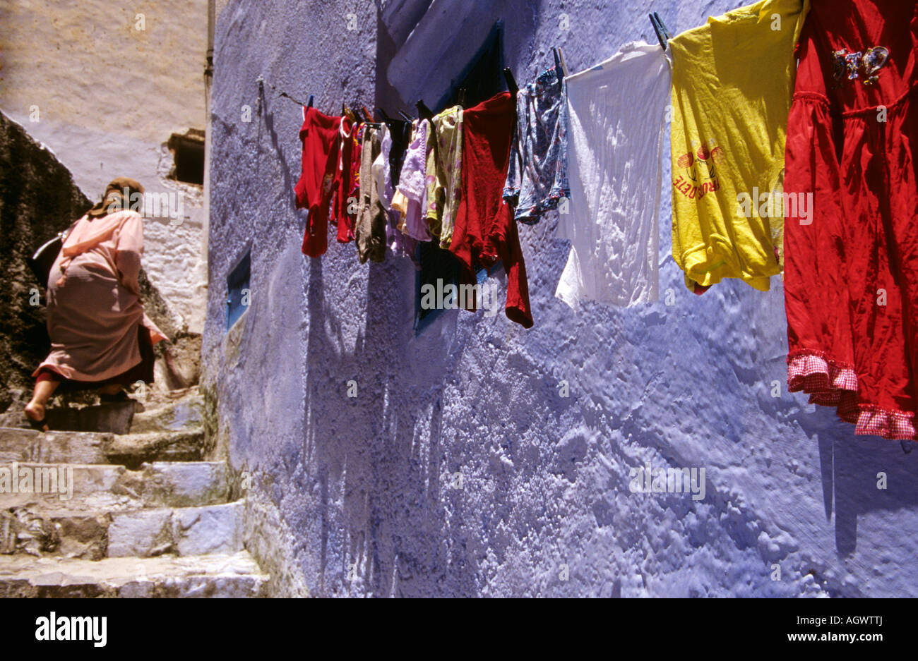 A woman walks up the stairs in Chefchaouen aka Chaouen with a clothes line in the foreground Stock Photo