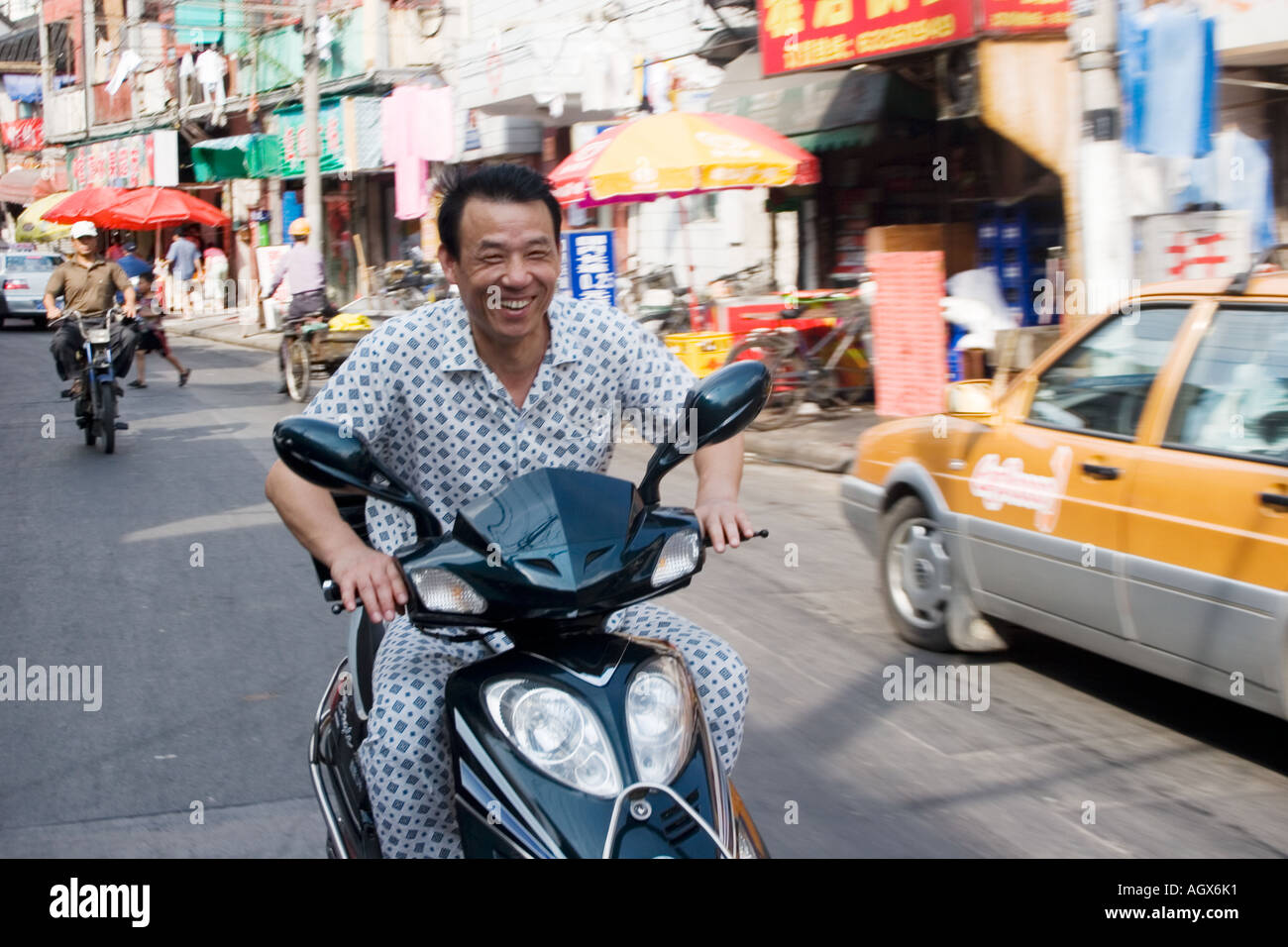 A man wearing pajamas rides his scooter down Fang Bang Lu. Pajamas are a common sight on Shanghai's streets. Stock Photo