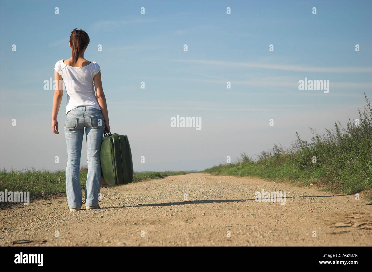 Young woman carrying suitcases on country road rear view Stock Photo