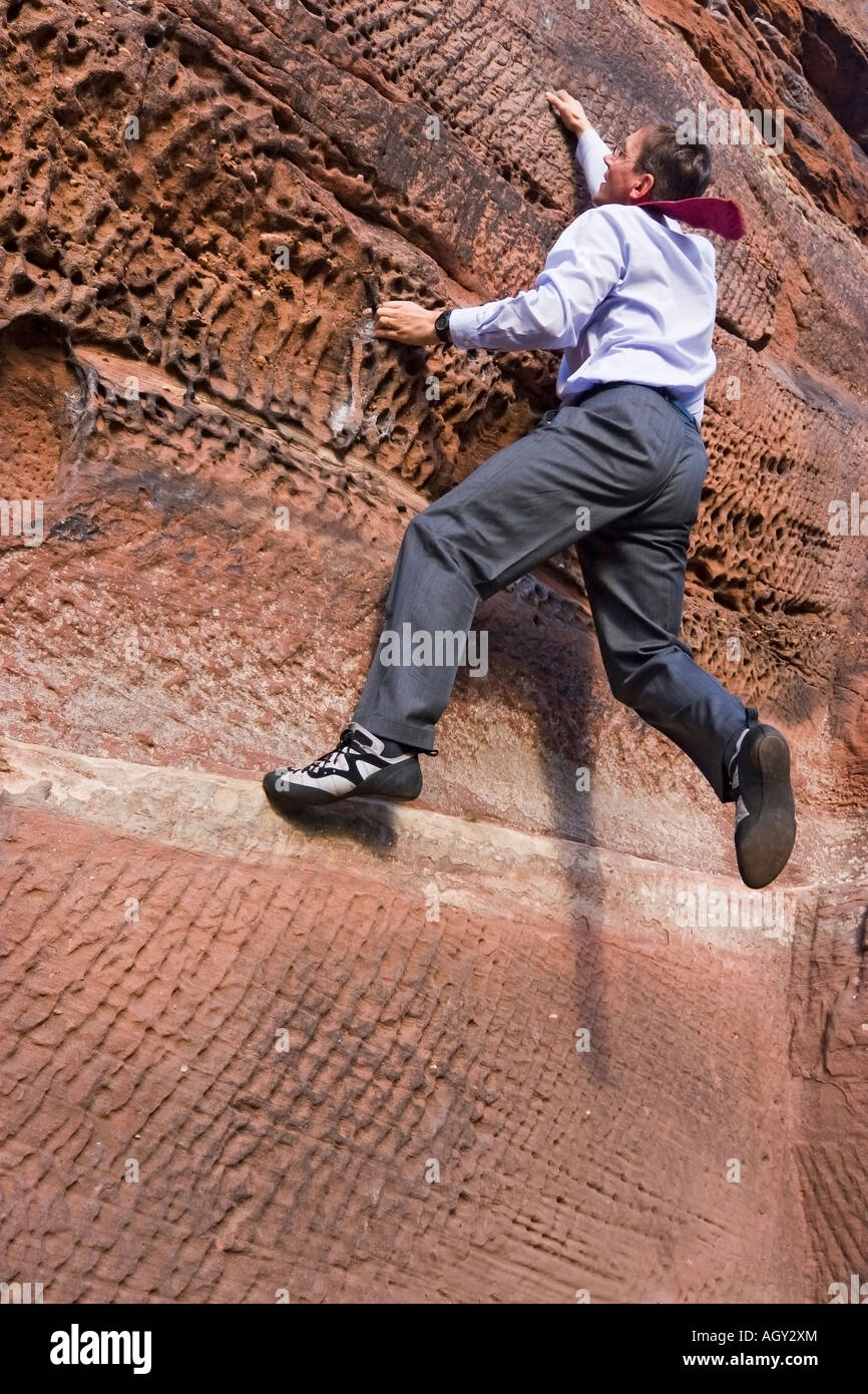 Businessman with cravat climbing a rock Stock Photo