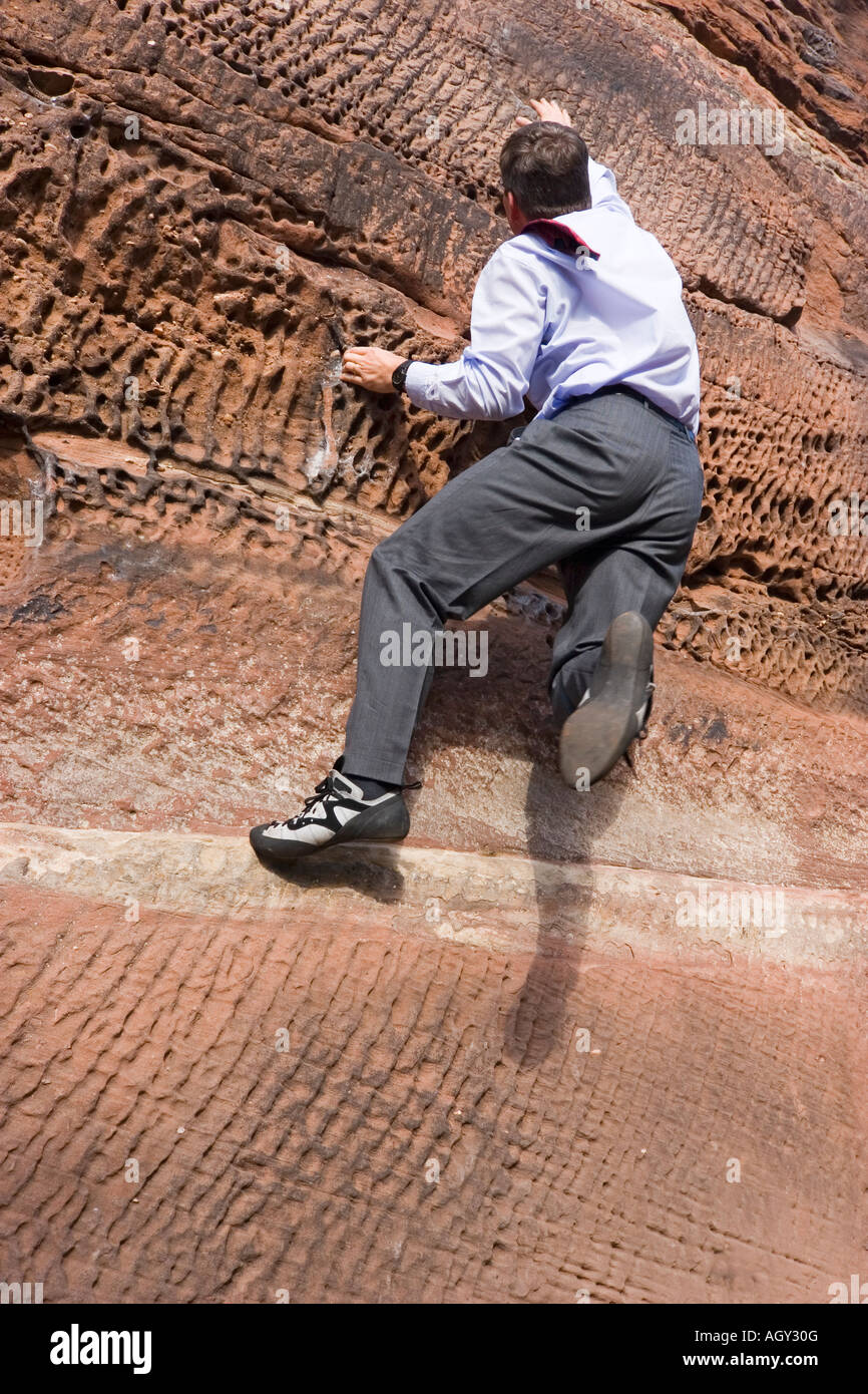 Businessman with cravat climbing a rock Stock Photo