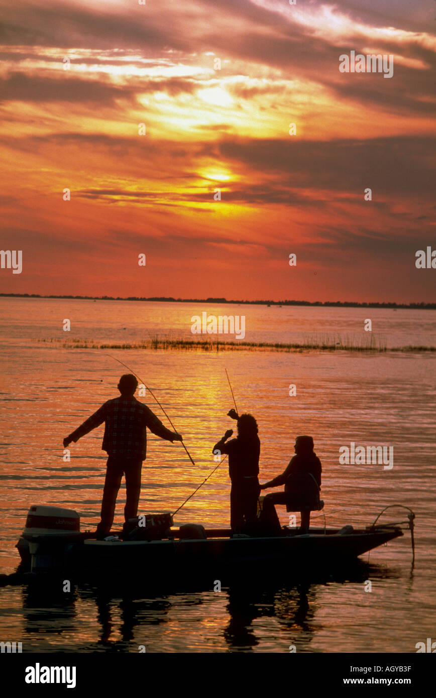 Family fishes for bass from a boat at sunset on Lake Okeechobee Florida Stock Photo
