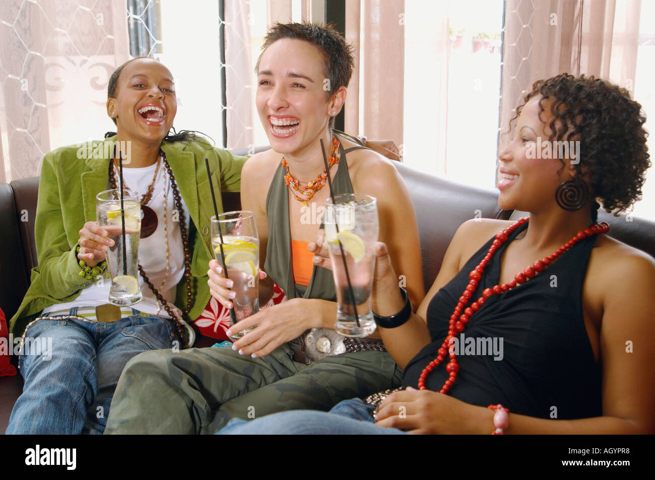 Three women laughing and drinking on sofa Stock Photo