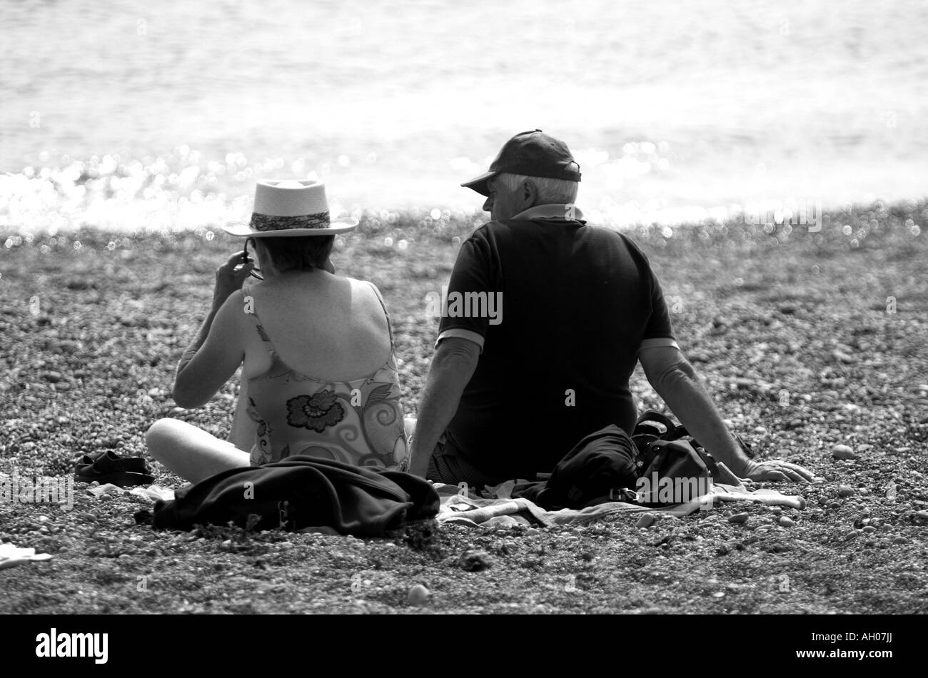couple on a beech sitting looking out to sea black and white Stock Photo