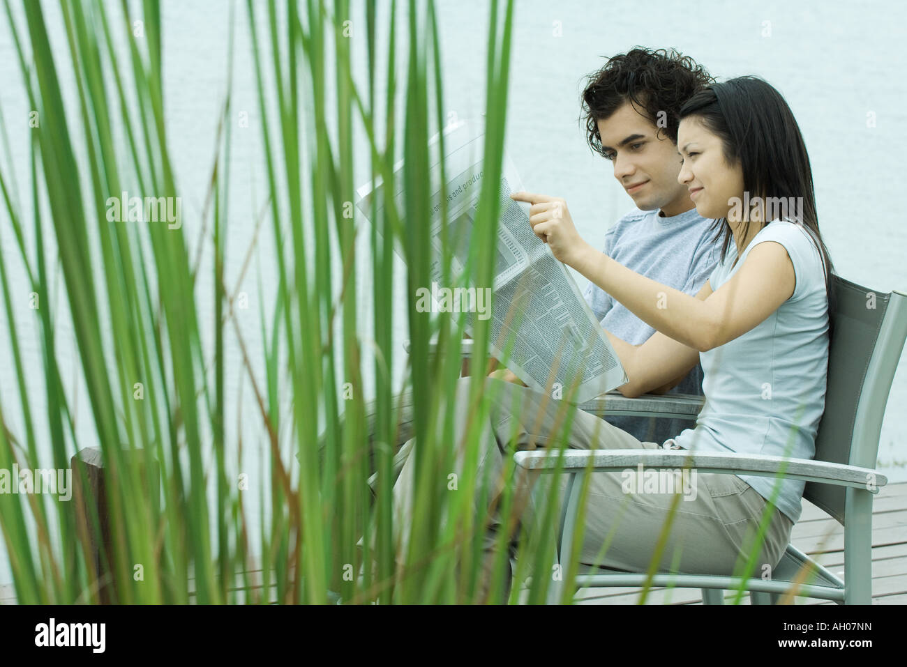 Young couple reading newspaper together by edge of lake Stock Photo