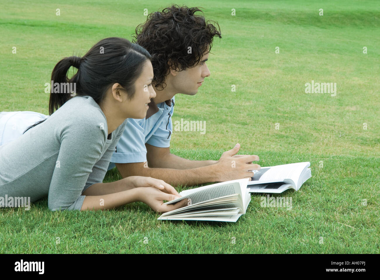 Young couple lying on grass with books, looking out of frame Stock Photo
