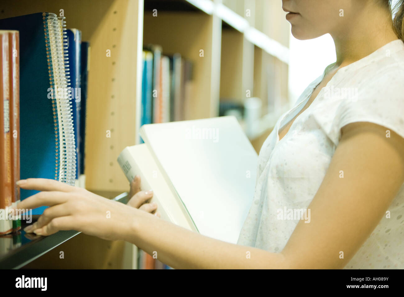 Young woman reaching for books on shelf in library, cropped view Stock Photo