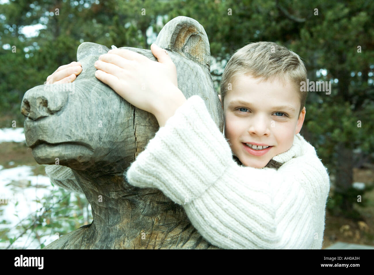 Boy embracing bear statue, covering its eyes with his hands, smiling at
