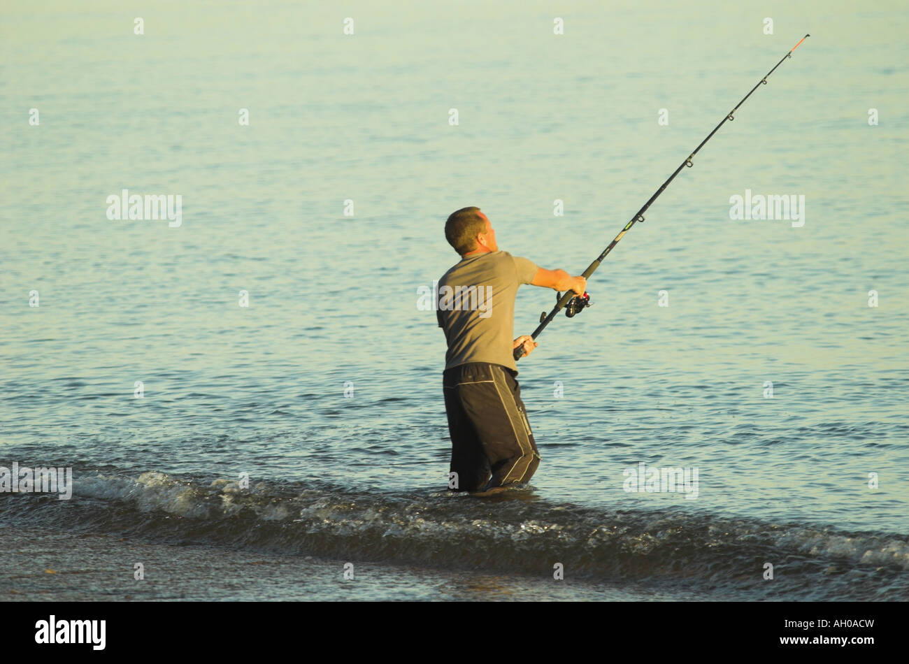 a lone fisherman casts out sea with the sun on his side Stock Photo