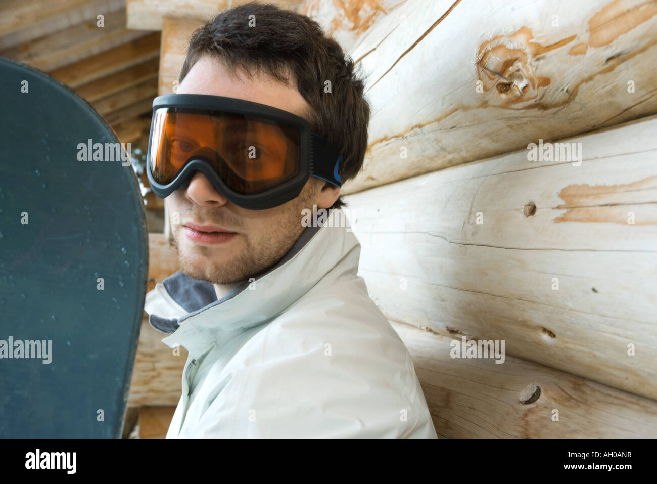 Young man with snowboard, looking at camera through ski goggles Stock