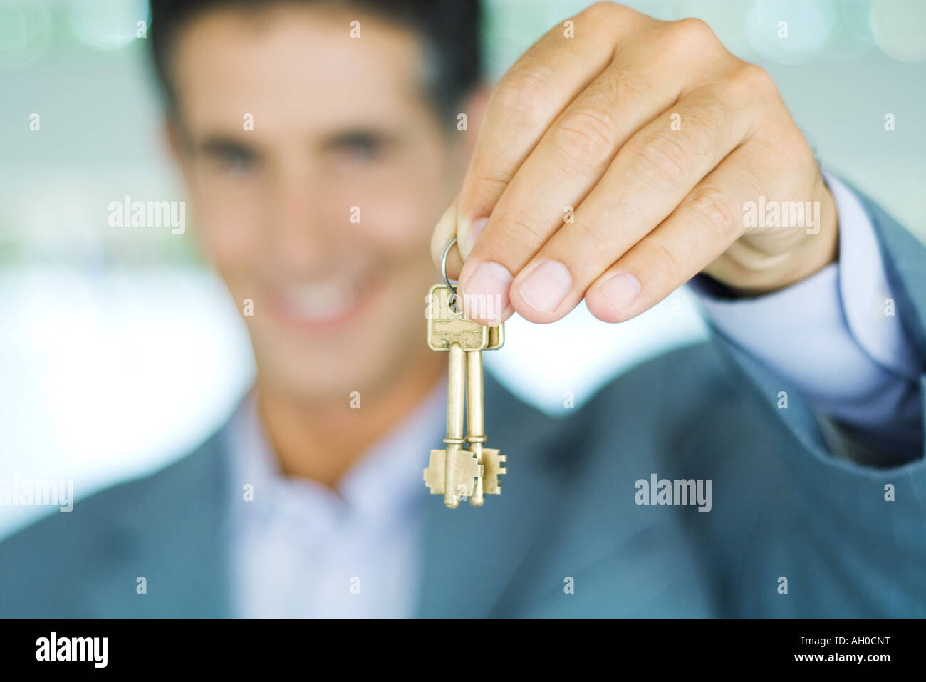 Man in suit holding up keys, focus on hand holding keys in foreground