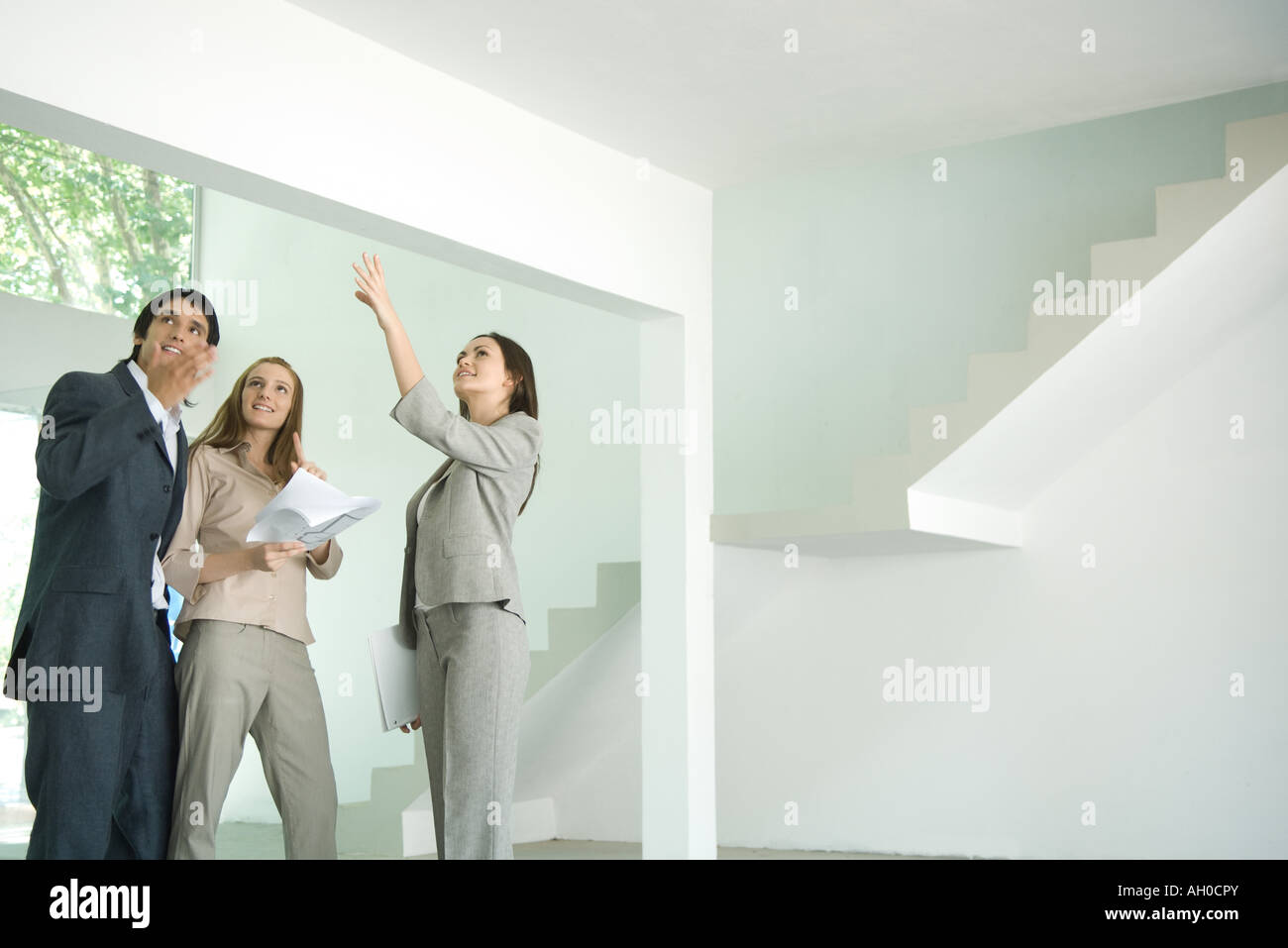 Female real estate agent standing in empty home interior with young couple, full length Stock Photo