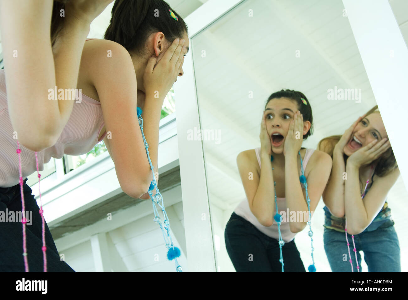 Two young friends bending over, looking at selves in mirror, hands on faces Stock Photo