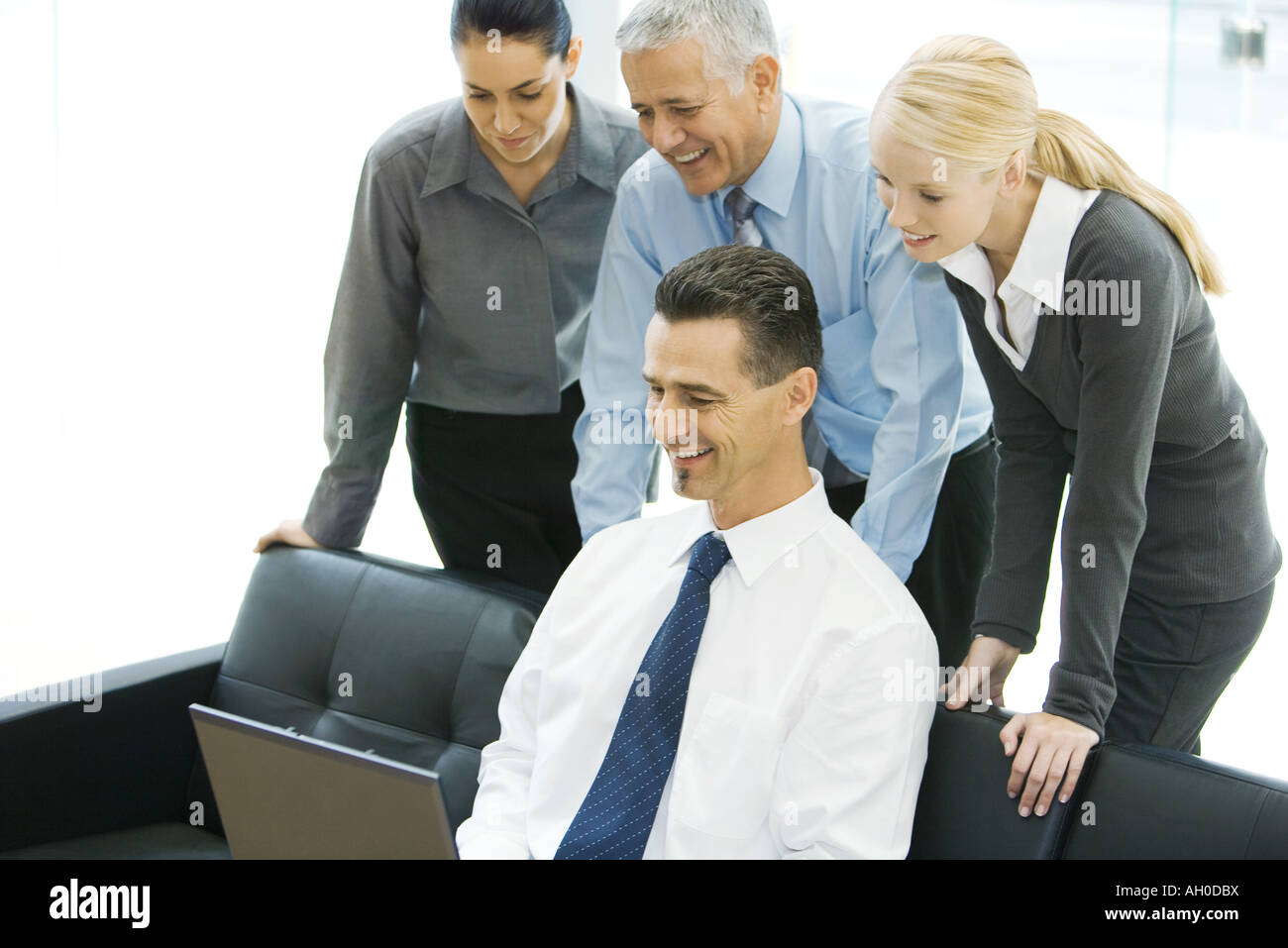 Businessman using laptop while colleagues look over shoulder Stock Photo