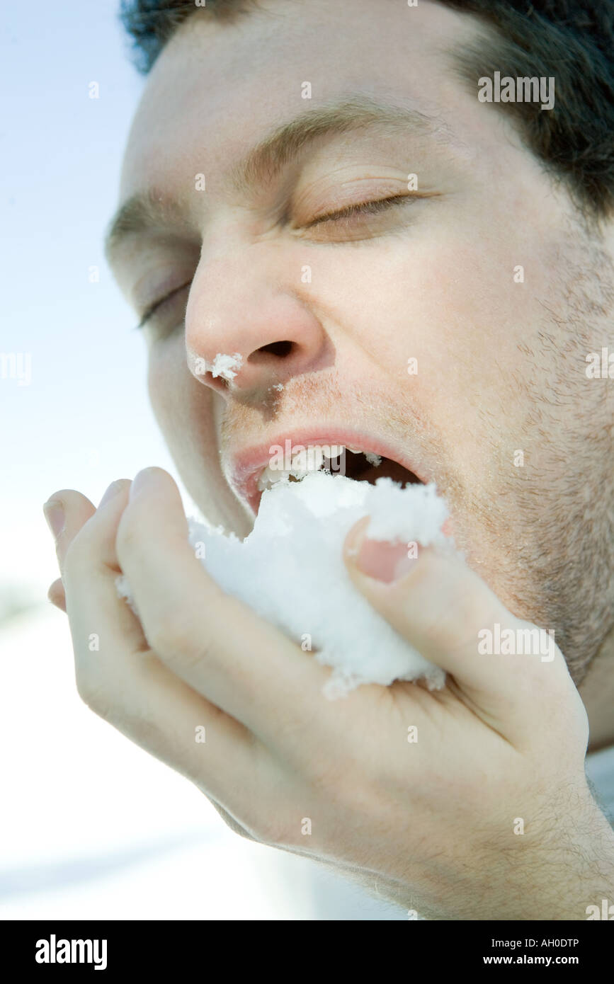 Young man eating snow, eyes closed, close-up Stock Photo