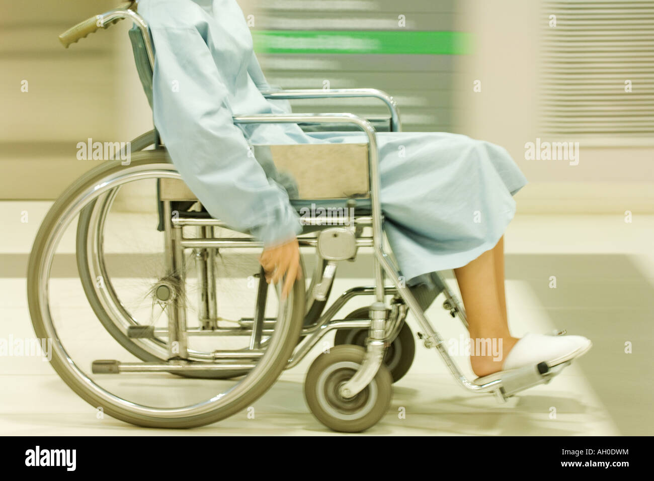 Cropped view of man using wheelchair, dressed in hospital gown, blurred