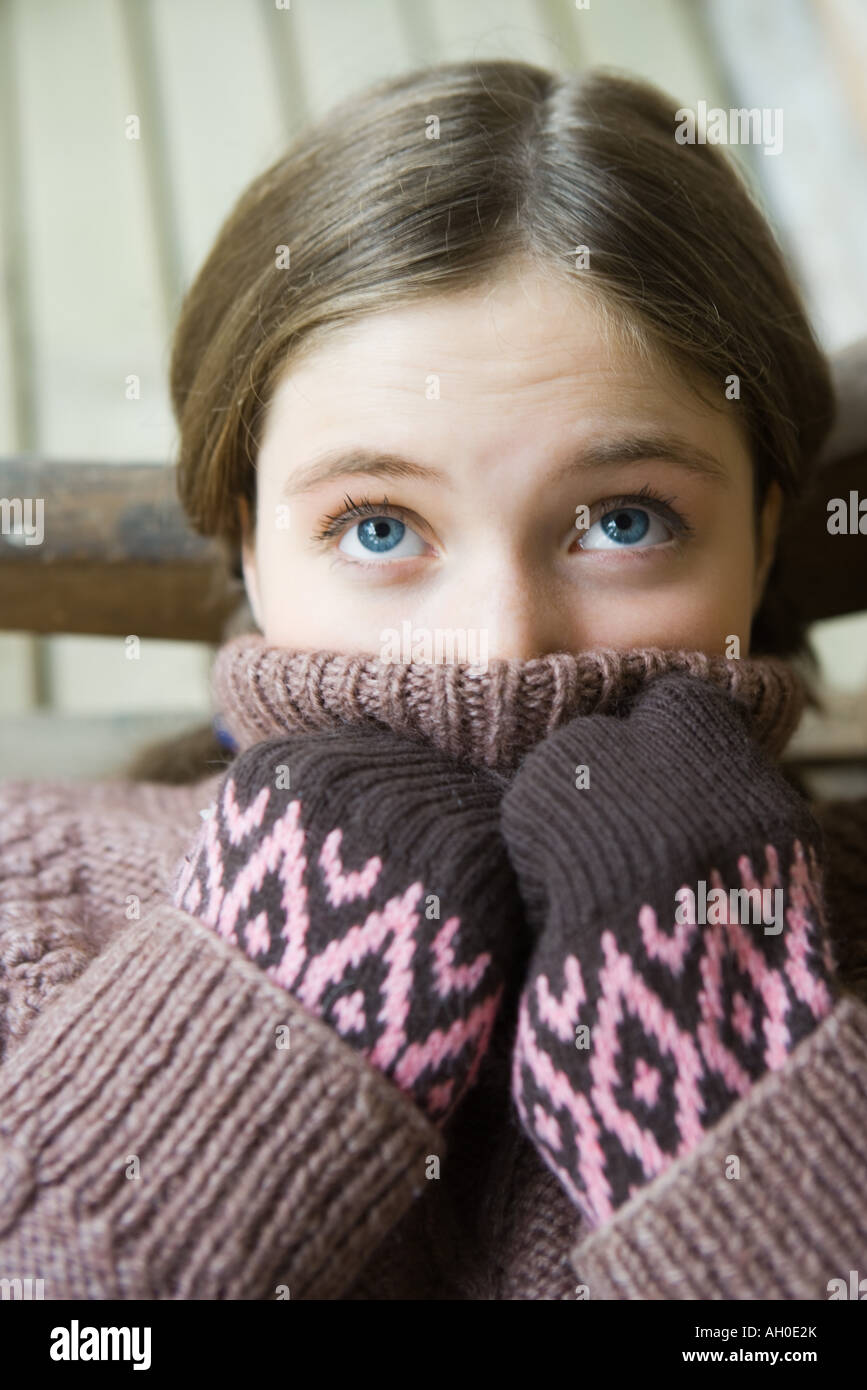 Teenage girl holding turtleneck over mouth, looking up Stock Photo