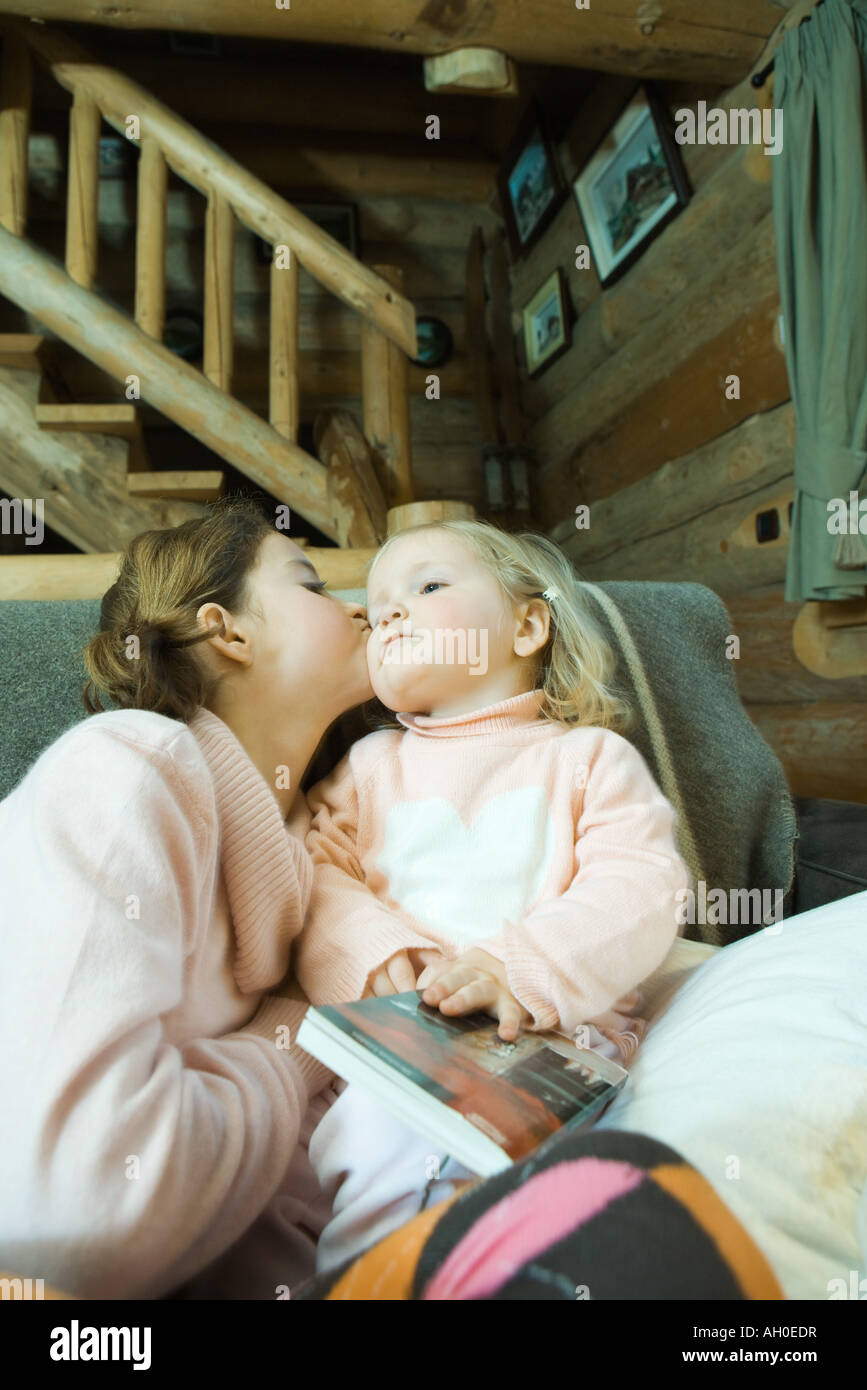 Girl and toddler sitting on couch, kissing cheek Stock Photo
