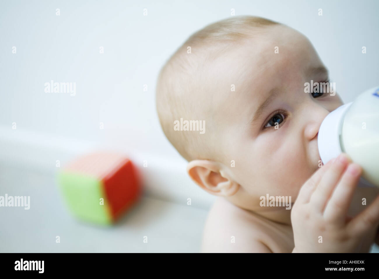 Baby drinking milk from bottle, looking away, head and shoulders Stock Photo