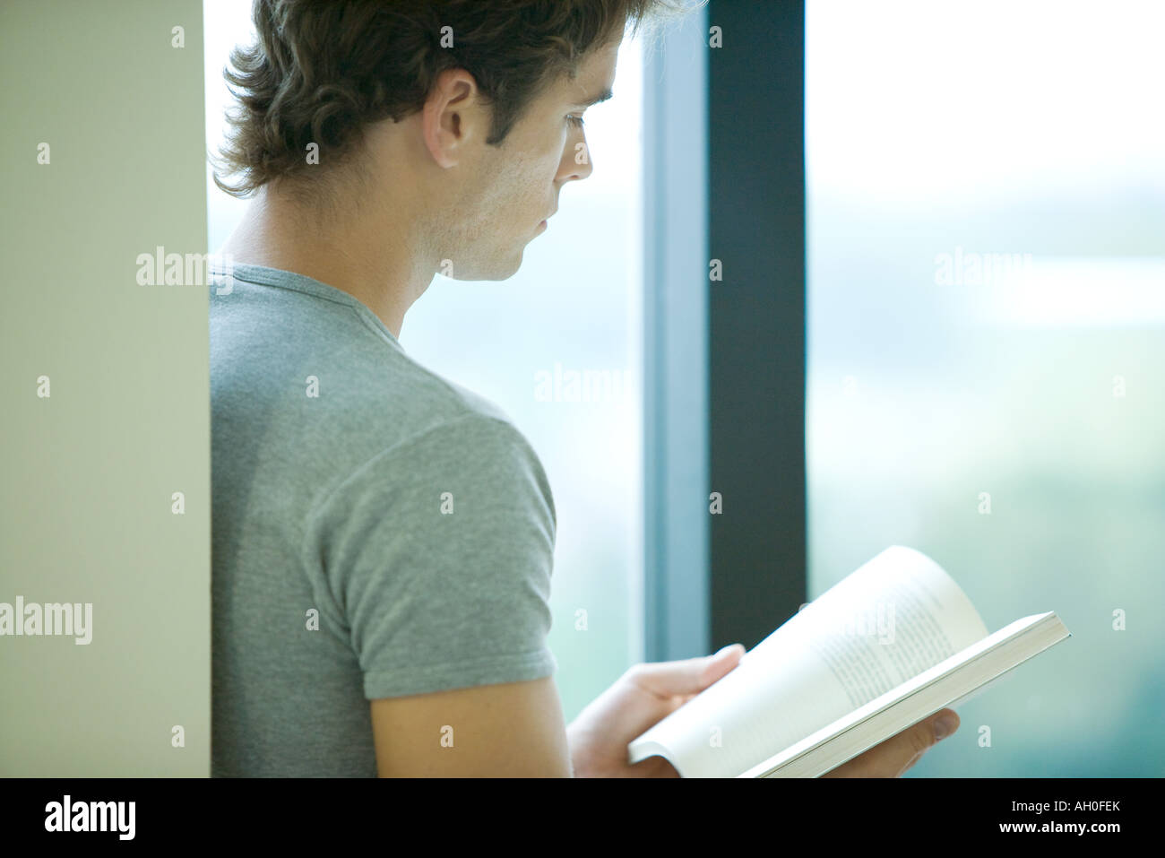 Young man reading book by window, side view Stock Photo