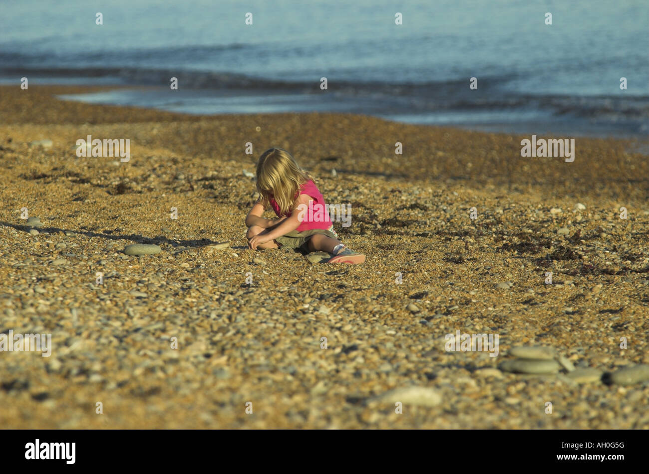 little girl sits playing on the beech on a summer evening Stock Photo