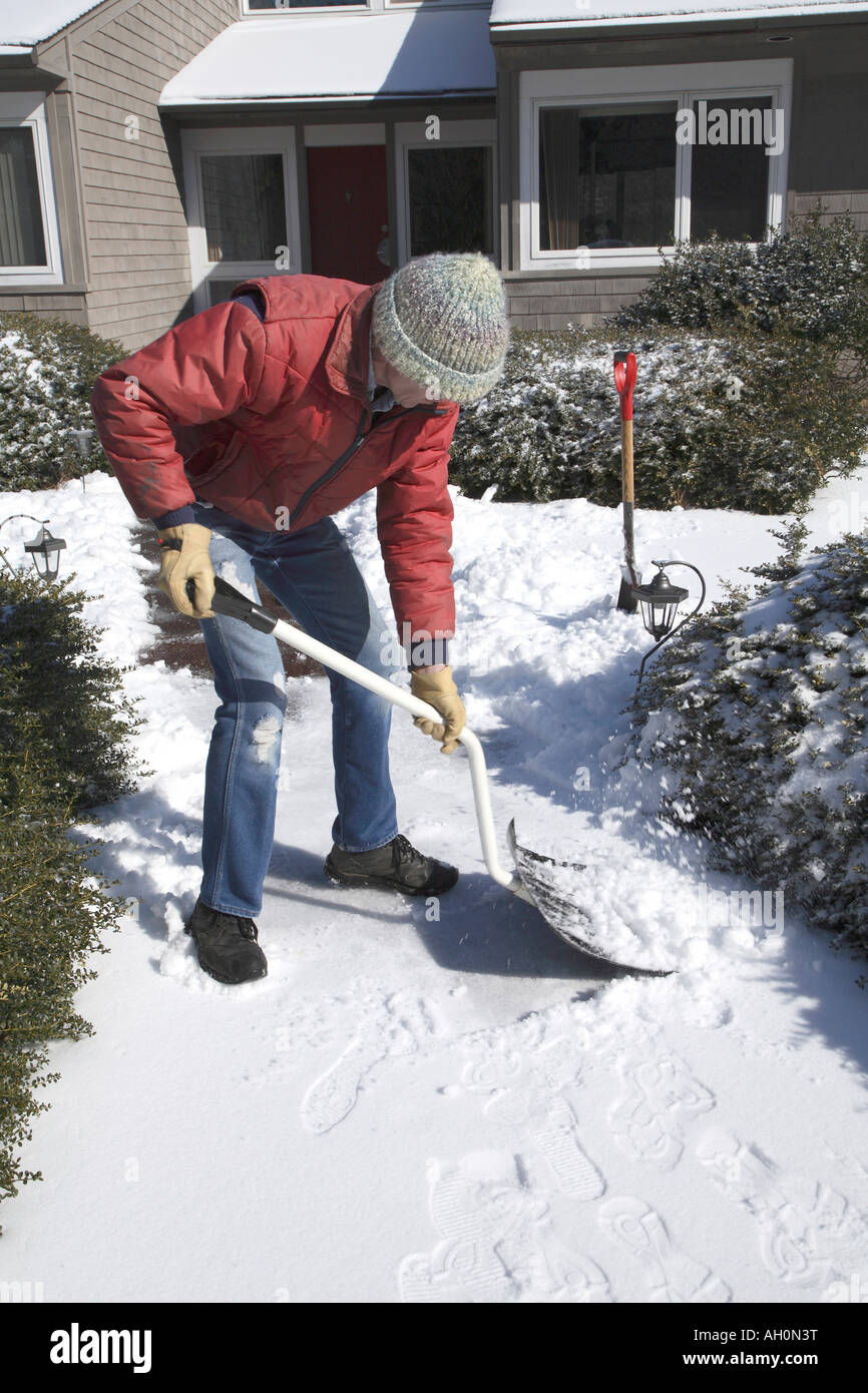 Man bent over and facing right using  bent handled snow shovel to scrape light covering of snow off to the right. Stock Photo