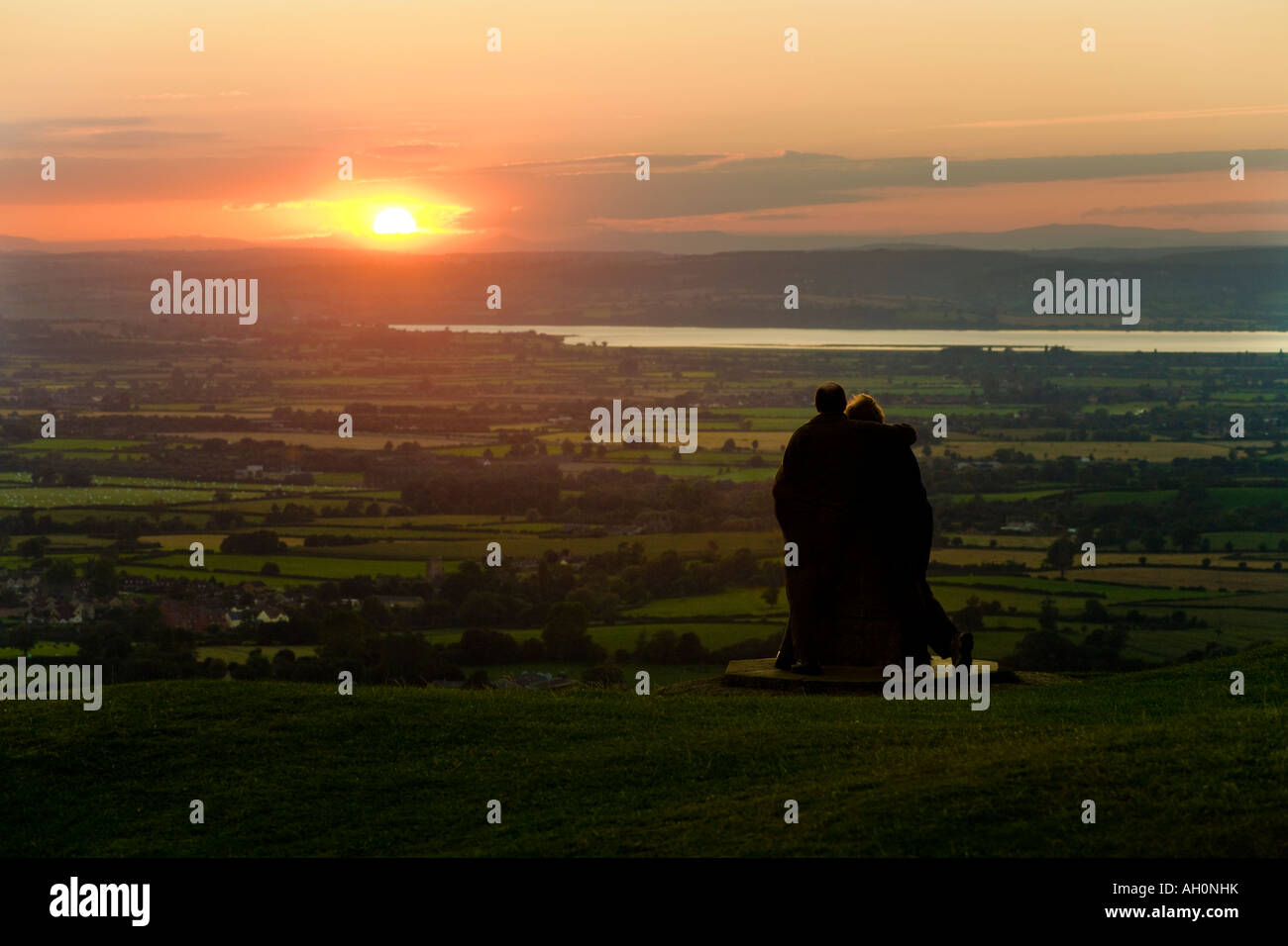 A couple watching the sunset from the Cotswold scarp viewpoint Frocester Hill adjoining Coaley Peak Picnic Site, Gloucestershire Stock Photo