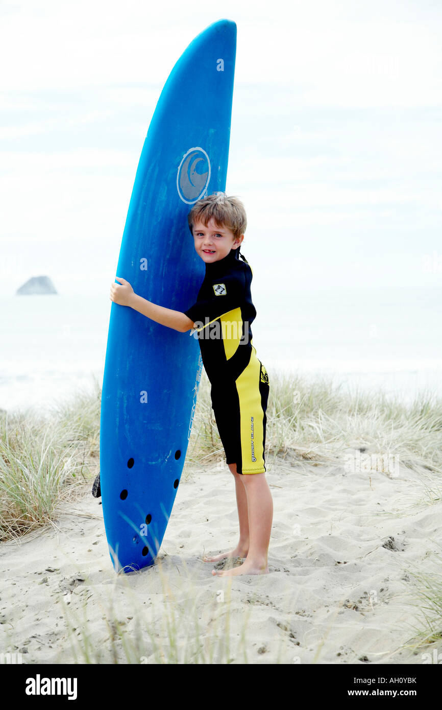 young boy in wetsuit carrying surfboard to the beach and looking at the