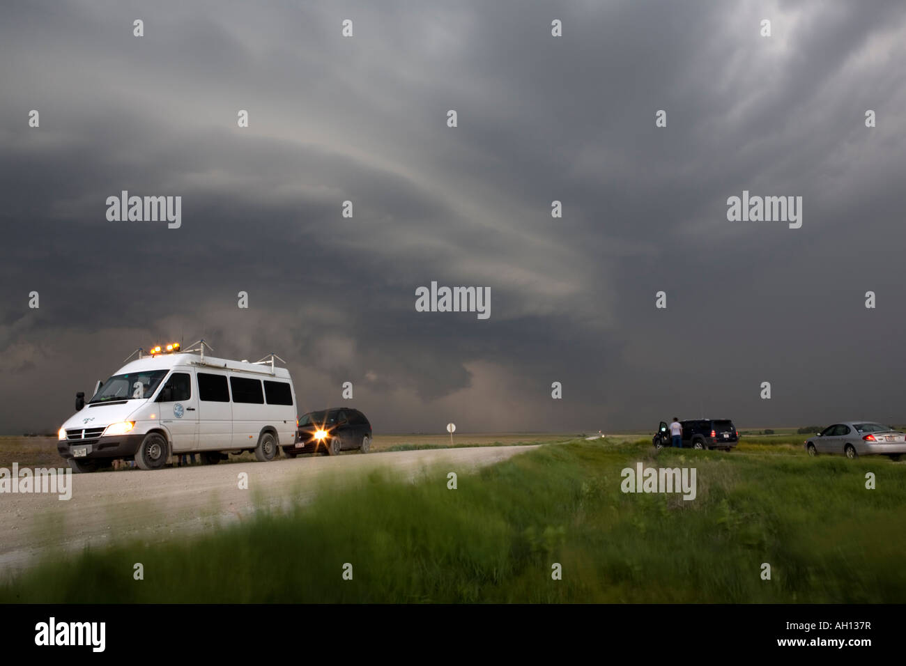 Storm chasers and their vehicles watch a supercell thunderstorm in Kansas USA on a rural dirt road Stock Photo