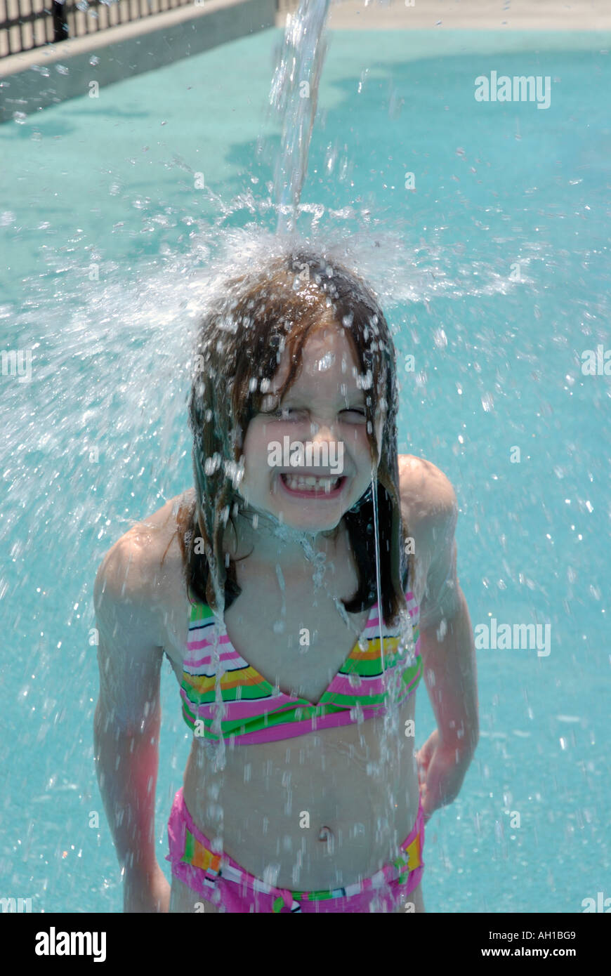 Young girl under water spout pouring water at playground in summer Stock Photo
